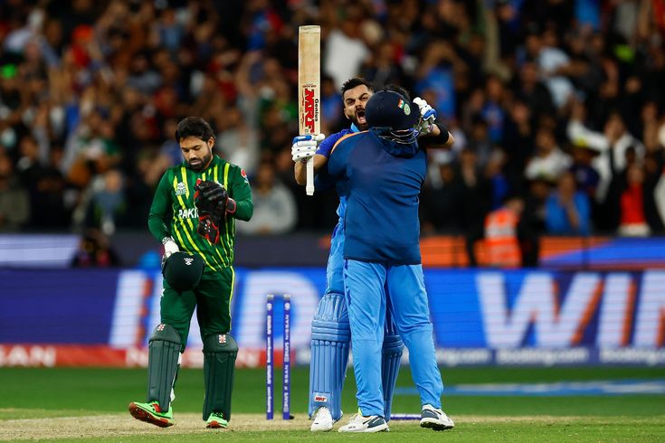 two men standing next to each other on top of a field holding cricket bats in their hands