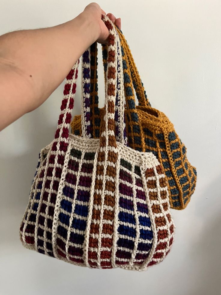 three crocheted purses being held by a person's hand on a white background