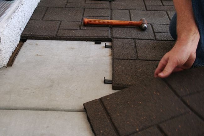 a man laying tile on the ground next to a brick wall with a hammer in it