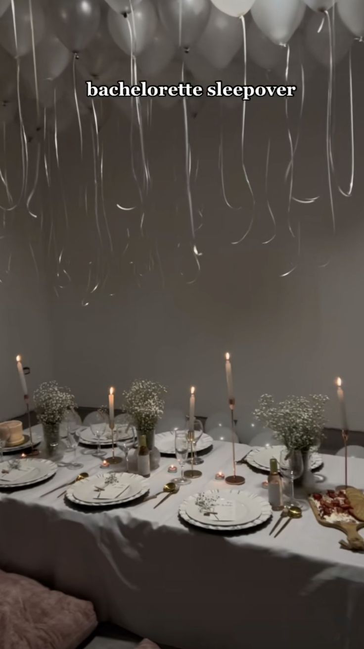 the table is set with white plates and silverware, candles, and balloon garlands