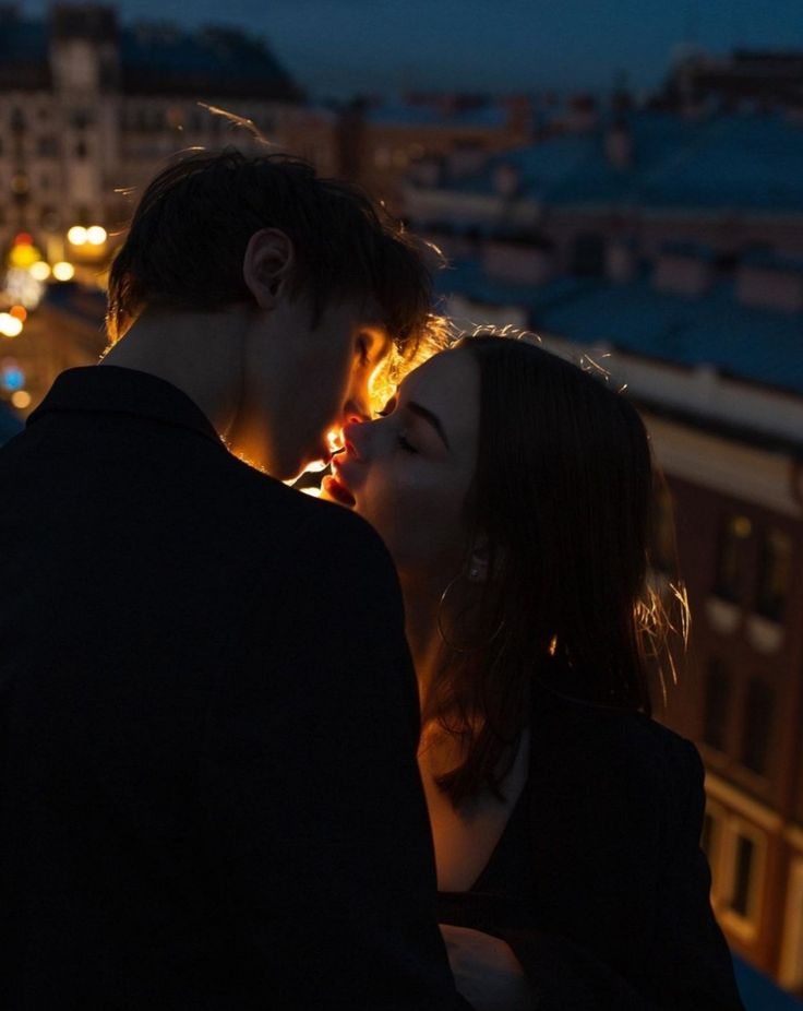 two people standing next to each other in front of a cityscape at night