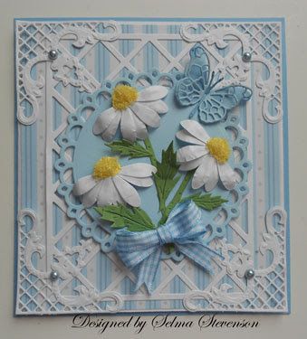 a card with white flowers and blue ribbon on it's side, in the shape of a heart