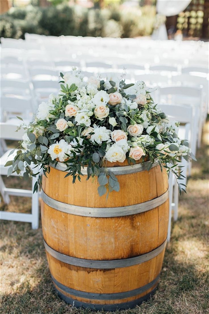 a wooden barrel with flowers and greenery on the top is set up for an outdoor ceremony