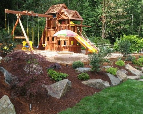 a wooden swing set in the middle of a garden with rocks and grass around it