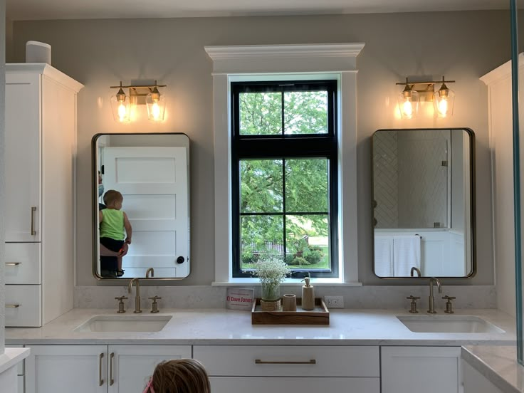 a young child standing in front of a bathroom window looking at the sink and mirror