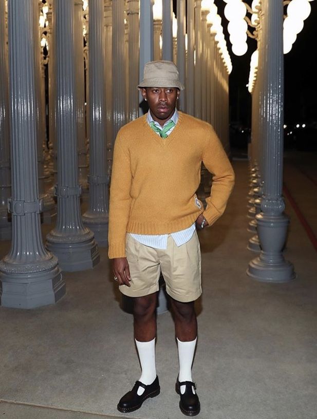 a man standing in front of columns wearing shorts and a sweater