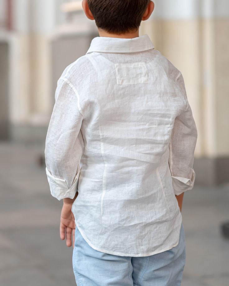 a young boy in white shirt and blue jeans walking down the street with his hand on his hip