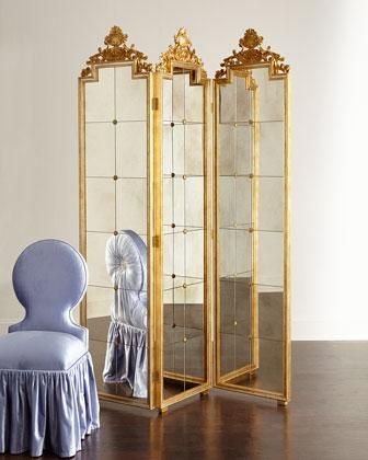 an ornately decorated room divider with a blue chair in the foreground and a gold framed mirror behind it