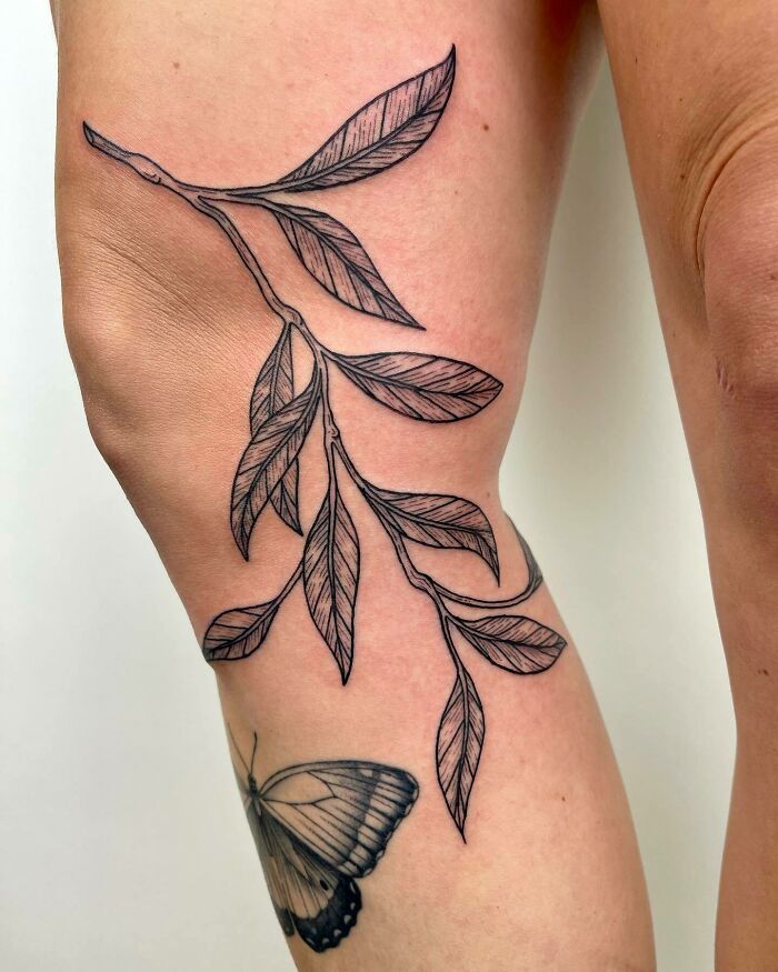 a woman's leg with a butterfly tattoo on it and leaves in the background