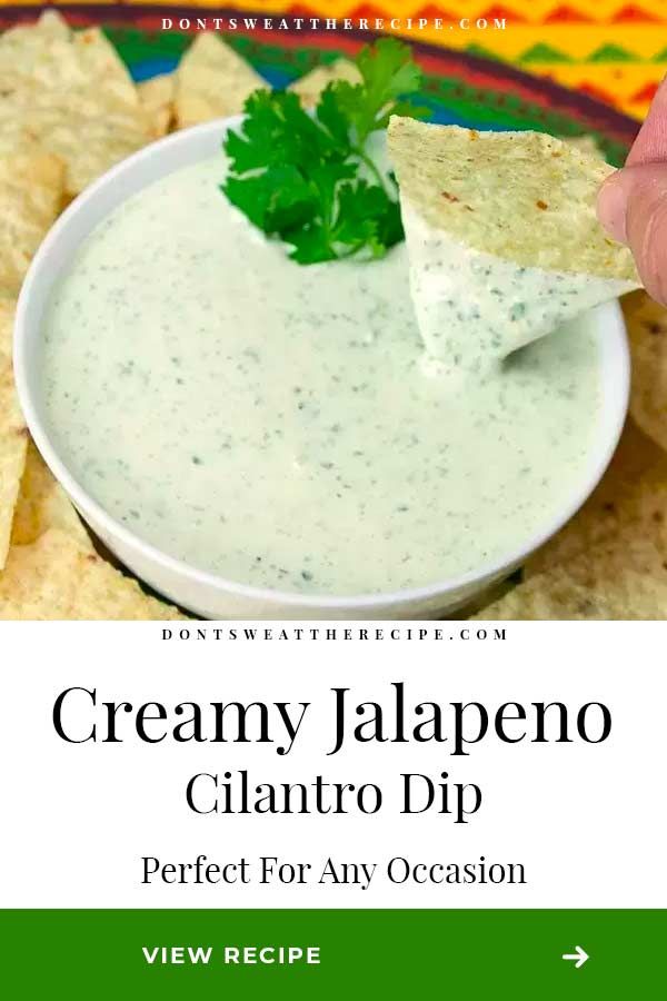 a hand dipping a tortilla chip into a bowl of creamy jalapeno cilantro dip