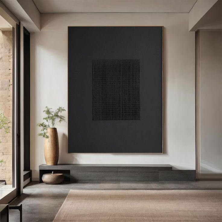 a large black painting hanging on the wall next to a vase and table with a plant in it