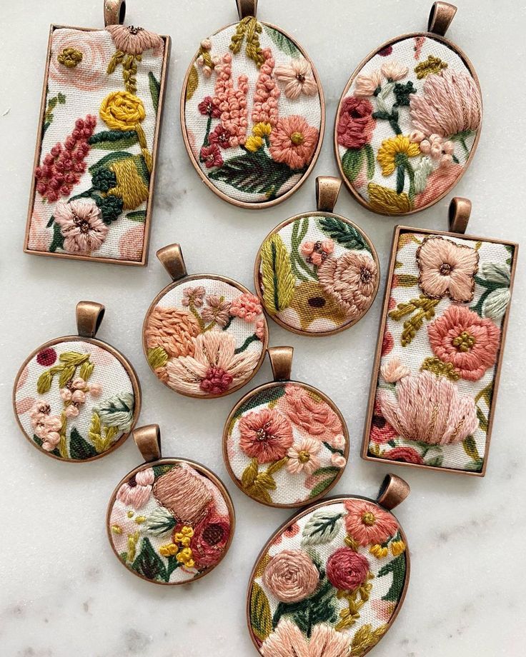 six embroidered pendants with flowers on them sitting on a marble counter top, all in different sizes and colors