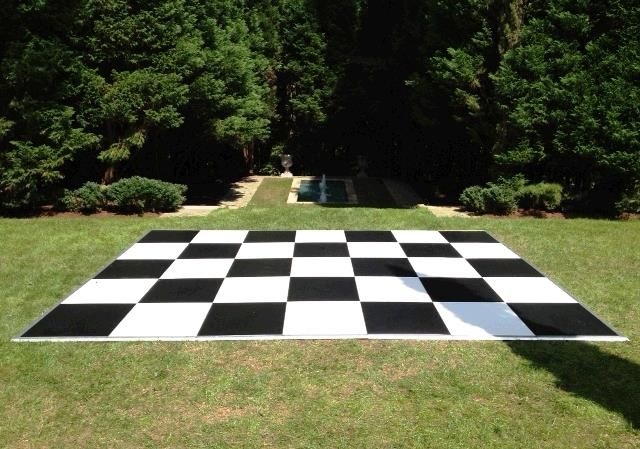 a large checkerboard board in the middle of a grassy area with trees behind it