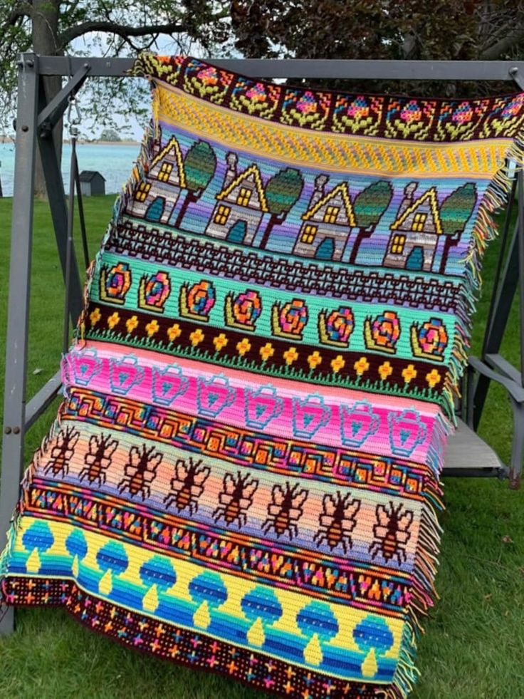 a multicolored blanket sitting on top of a metal stand in the grass next to a tree