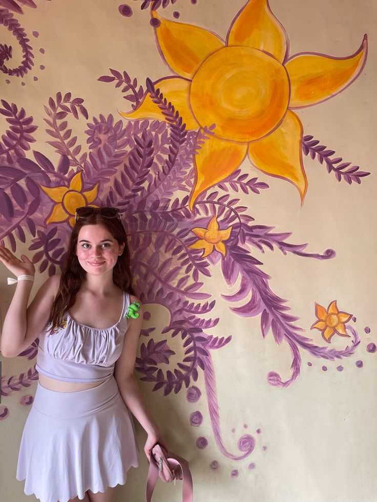 a young woman poses in front of a painted wall with purple flowers and yellow sunflowers