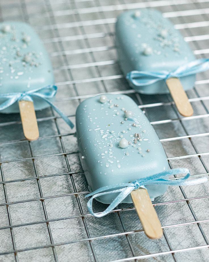 three popsicles with blue icing and sprinkles on them sitting on a wire rack