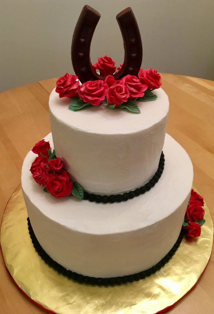 a three tiered cake with red flowers on it and a horseshoe shaped topper