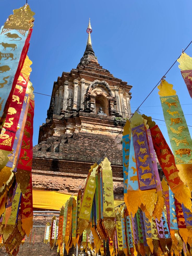 many colorful flags are hanging in front of a building with a steeple behind them