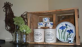 an old wooden box with blue flowers and tea cups in it on a table next to a vase