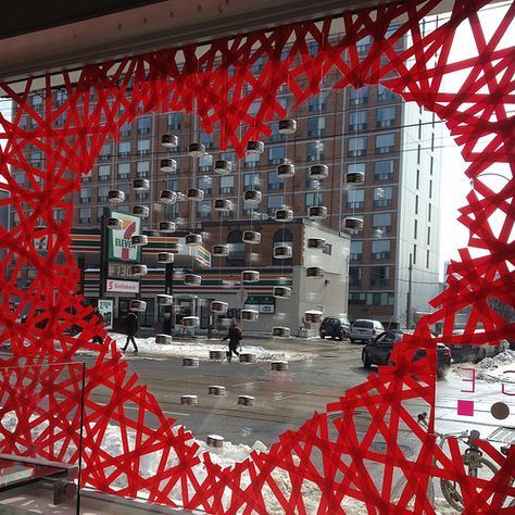 a large red sculpture in the middle of a city with buildings and cars behind it