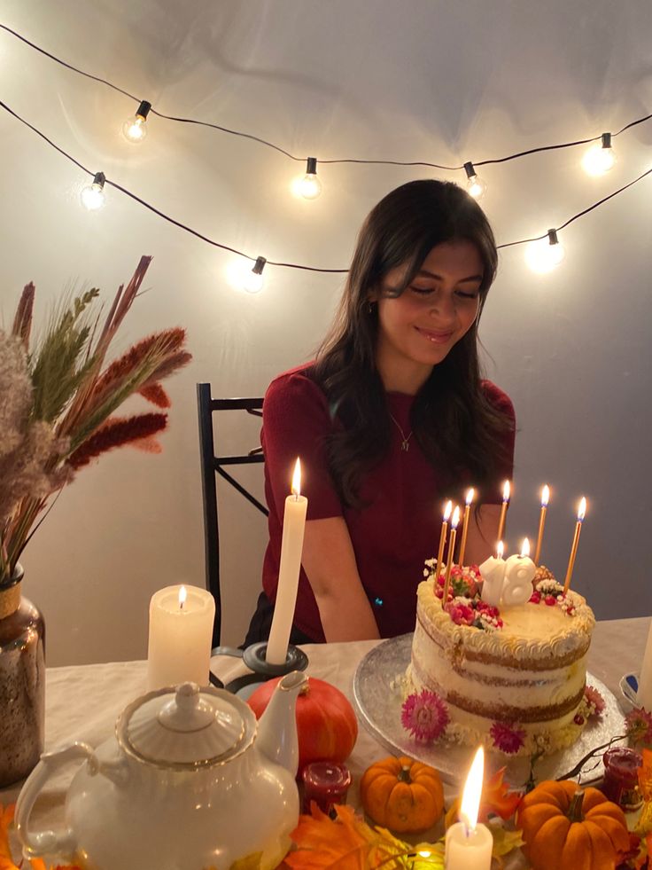 a woman sitting at a table in front of a cake with lit candles