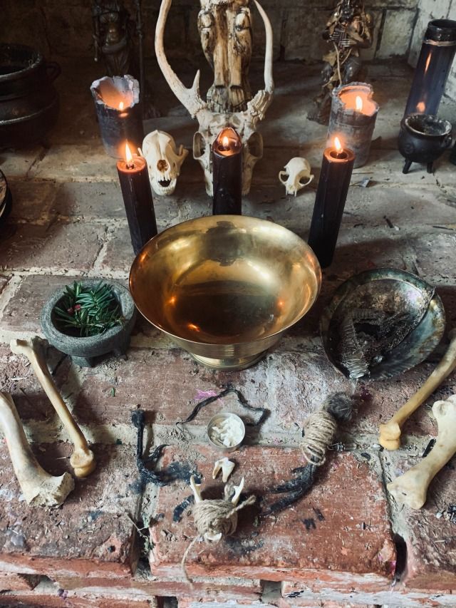 a table topped with candles and skulls on top of a brick floor next to a bowl