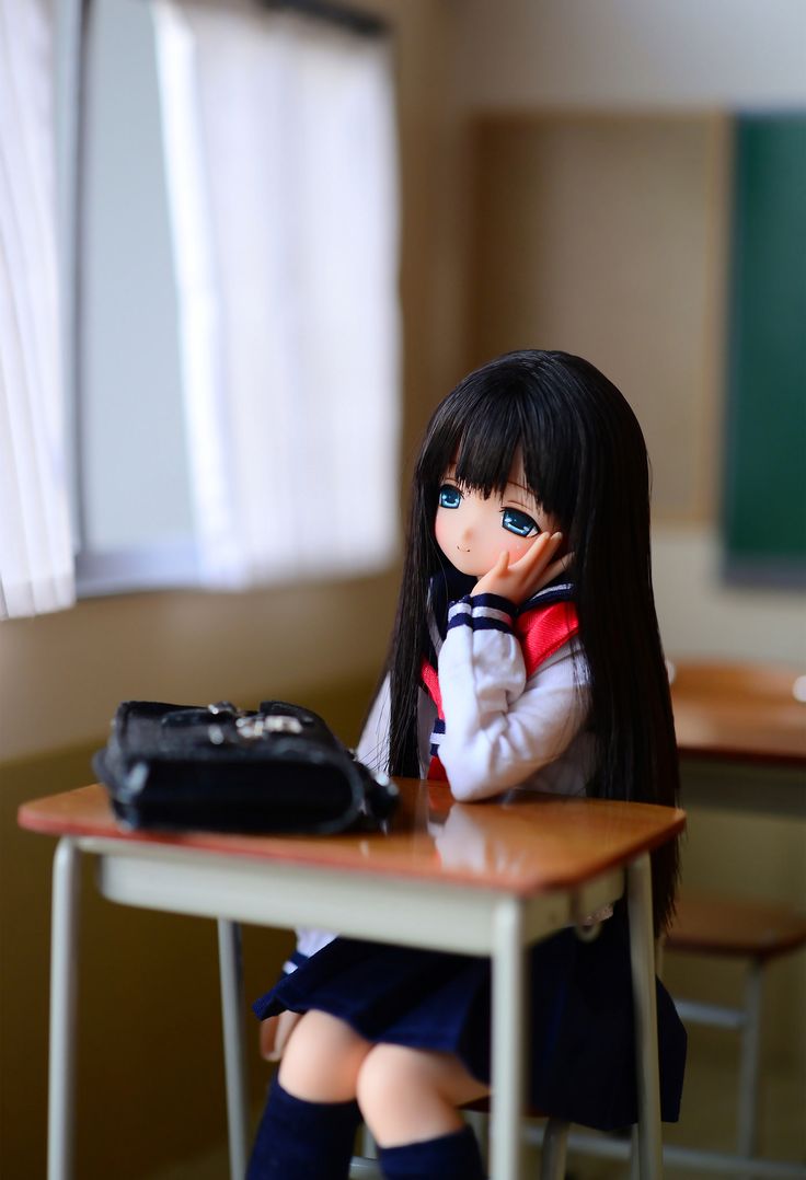 a doll sitting at a desk with a black bag on it's back legs