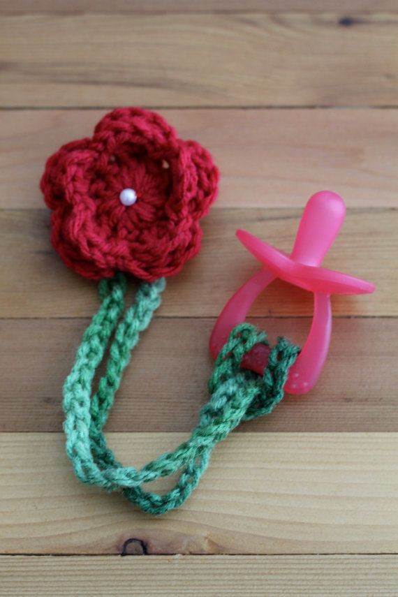 a crocheted flower with a pink object attached to it on a wooden surface