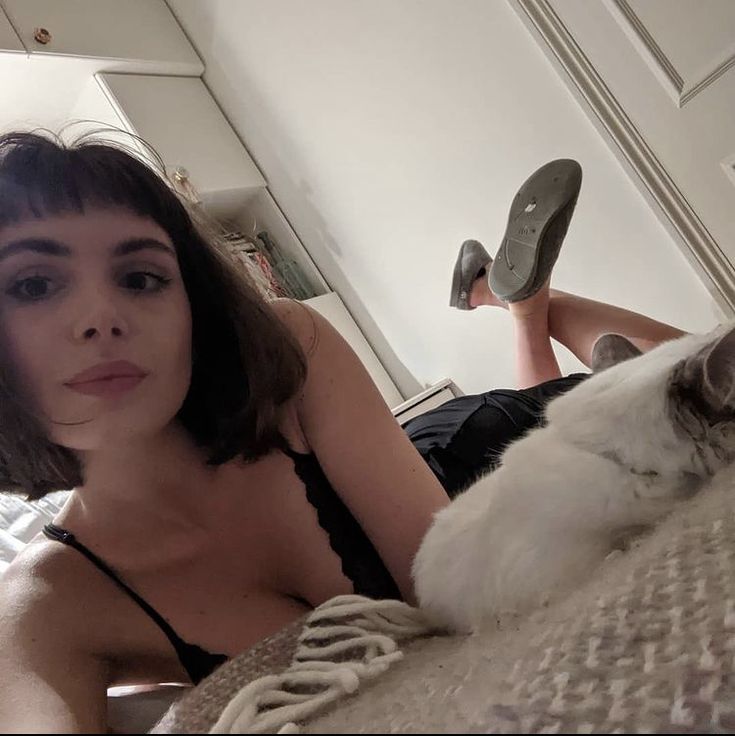 a woman laying on top of a bed next to a white and gray cat with her head up