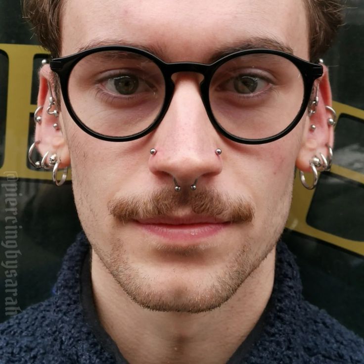 a man with piercings on his nose wearing glasses