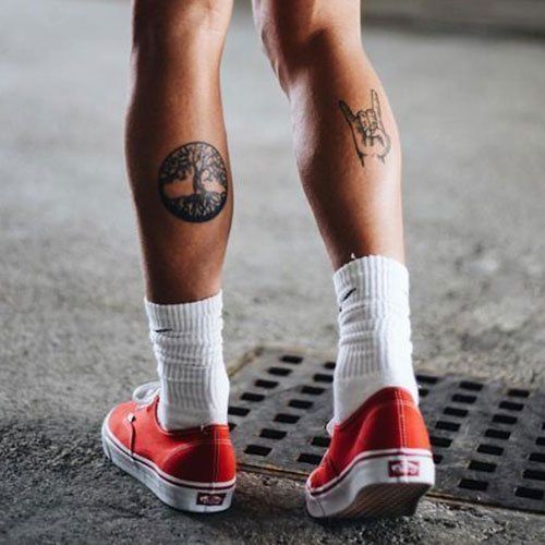 a person with tattoos on their legs standing on a skateboard