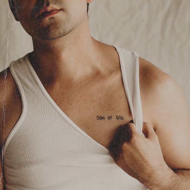 a man wearing a white tank top with the word son of god written on his chest