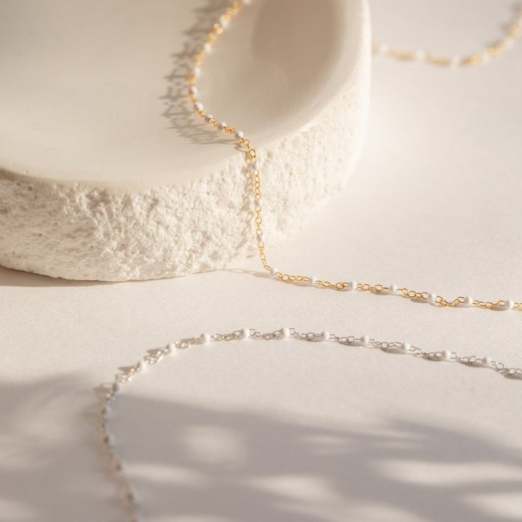 This beautifully versatile necklace is designed to catch attention. The soft hues and delicate beading of the White Station Necklace is perfect for everyday wear. Handmade with dainty white beads, this chain will bring a warm and modern touch to your outfit and is sure to become your new favorite go-to accessory. Material: High Quality Solid 925 Sterling Silver Finish: Sterling Silver ∙ 18K Gold Featuring a dainty Beaded Necklace with ~2mm White Beads spaced ~5mm apart, with adjustable 16 to 18 Initial Tag Necklace, Dainty Initial Necklace, Demi Fine Jewelry, Name Jewelry, Station Necklace, Shopping Ideas, White Beads, Bar Necklace, Tag Necklace