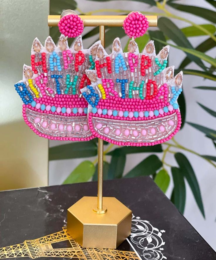 a pink and blue tiara sitting on top of a gold stand next to a plant