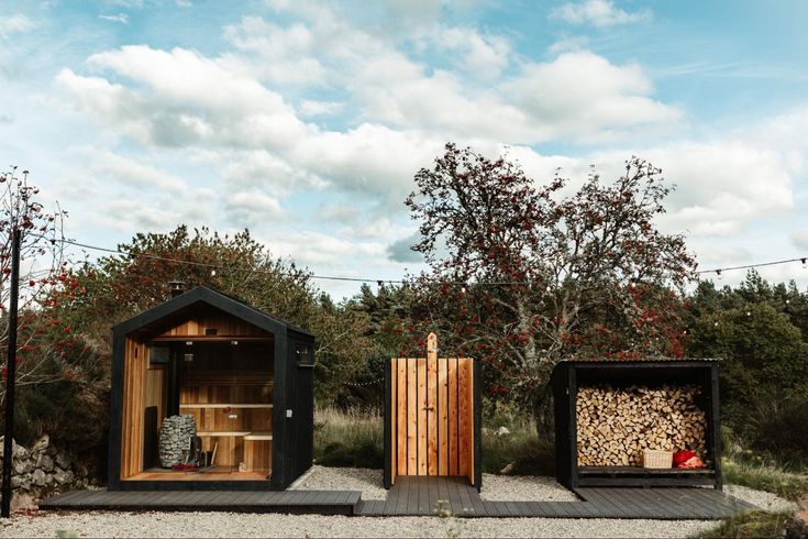 two small wooden buildings sitting on top of a gravel field next to trees and bushes