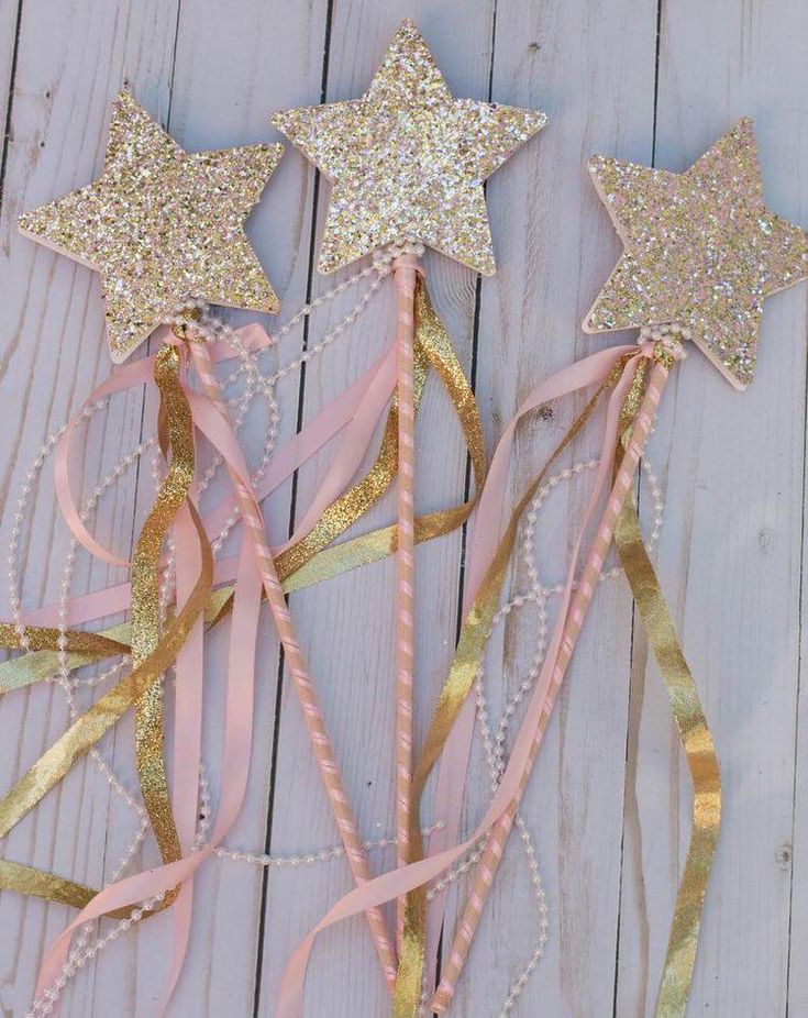 three pink and gold star wands on a white wooden surface with ribbons in the shape of stars