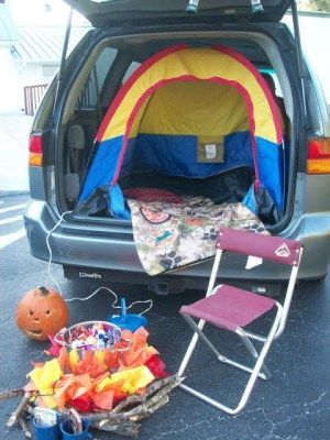 the back end of a car with its trunk open and camping gear set up next to it