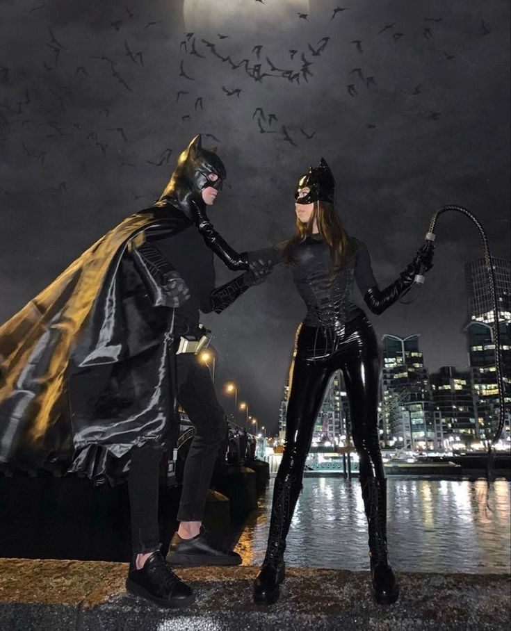 two people dressed up as batman and catwoman standing next to each other in front of a city at night