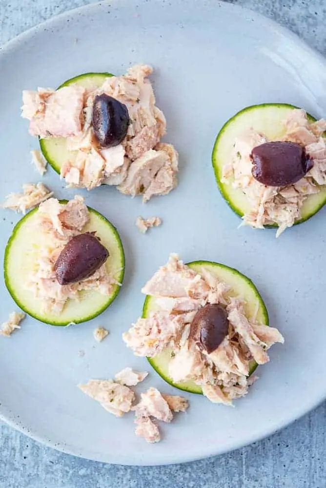 four pieces of cucumber with tuna and olives on them sitting on a white plate