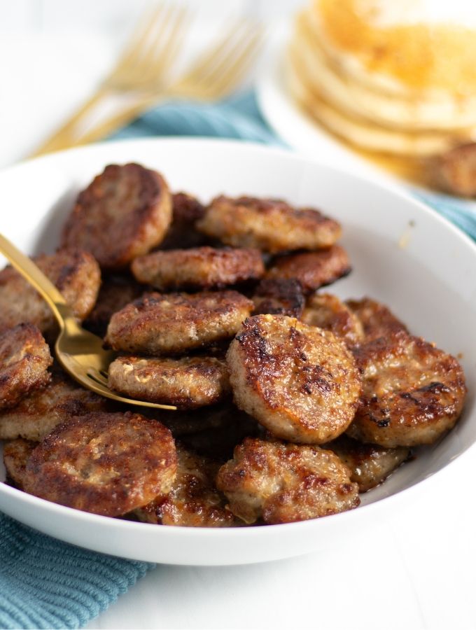 a white bowl filled with fried sausages on top of a blue and white table cloth