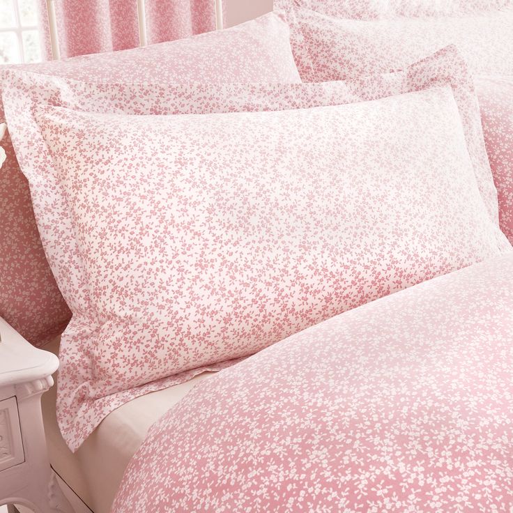 a bed with pink sheets and pillows on top of it next to a night stand