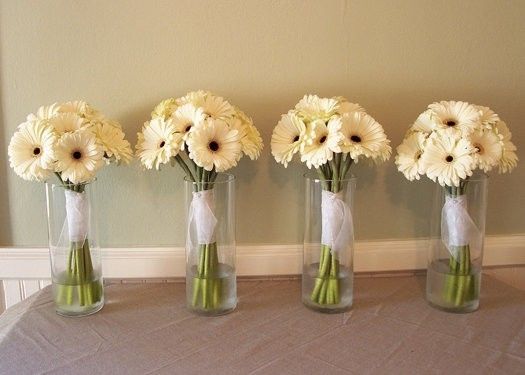 four vases with white flowers in them sitting on a table cloth covered tablecloth