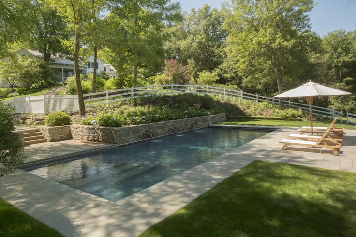 a swimming pool surrounded by landscaping and trees in the back yard with an outdoor grill area