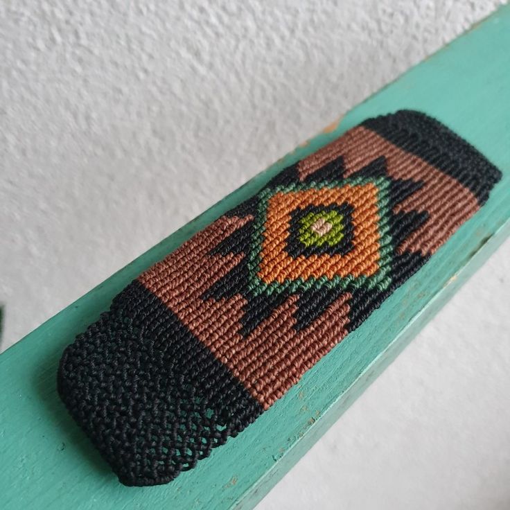 a knitted cell phone case sitting on top of a green wooden bench next to a white wall