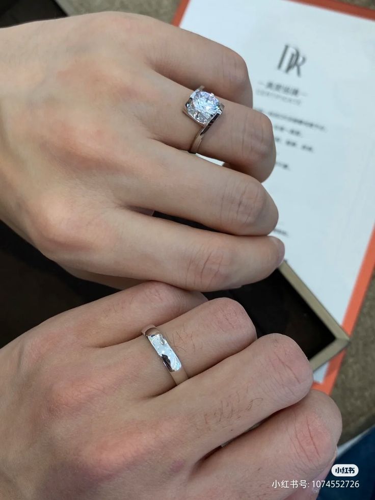 two hands holding each other with wedding rings on top of their fingers and an open book in the background