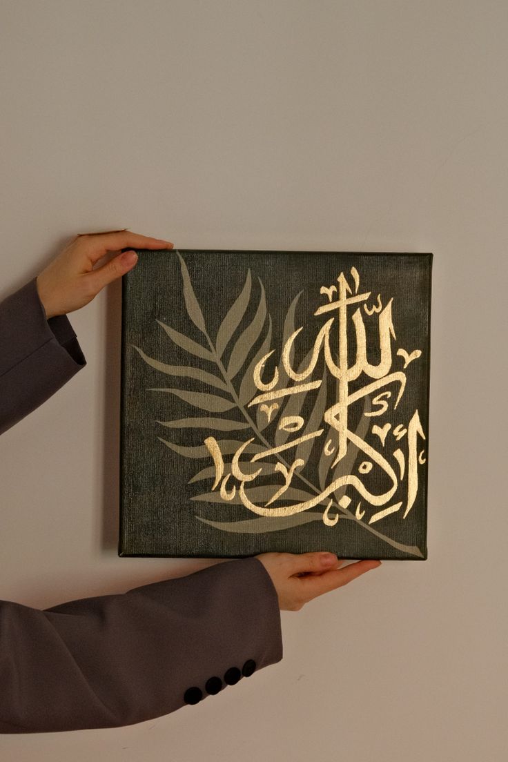 a person holding up a piece of art with arabic writing on it