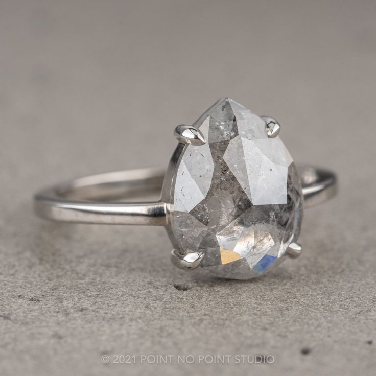 a large gray diamond ring sitting on top of a cement surface with the center stone missing