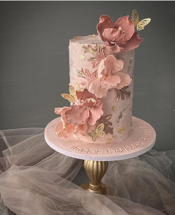 a three tiered cake with pink flowers and butterflies on the top is sitting on a gold pedestal