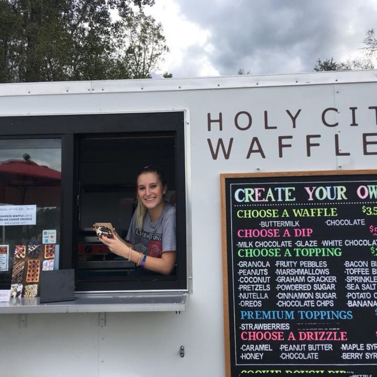 a woman standing in the window of a food truck with menus on it's side