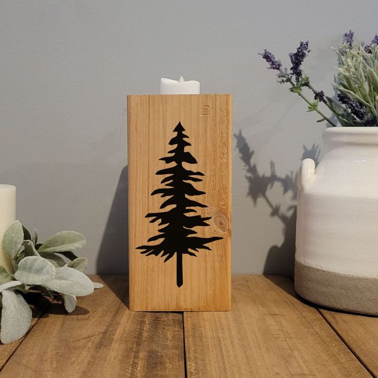 a wooden candle holder with a pine tree design on it next to some flowers and candles